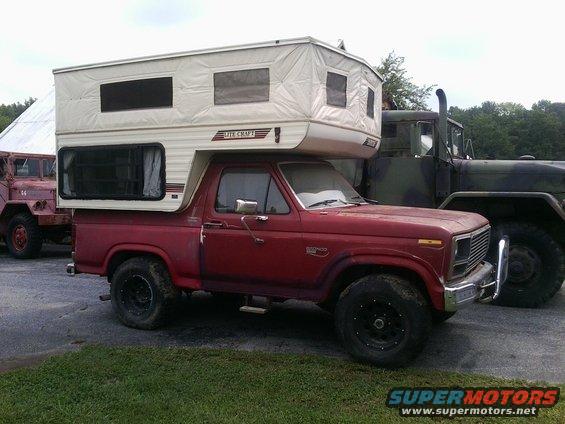 Red Ford Bronco with a white pop-up camper shell, seen from the front-right