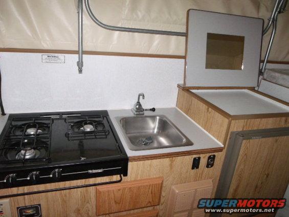 Camper interior with a black two-burner stove, stainless steel sink, and faucet