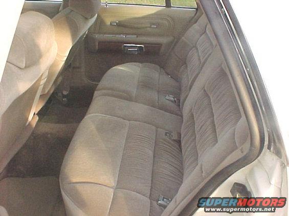 Back seat and door panel of a car interior. Tan fabric seats with horizontal pleats. Wood trim on door panel