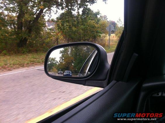 Side mirror view from inside a car, showing trees and road in the reflection