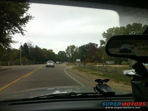 View from inside a vehicle looking out at a wet road with trees lining the sides