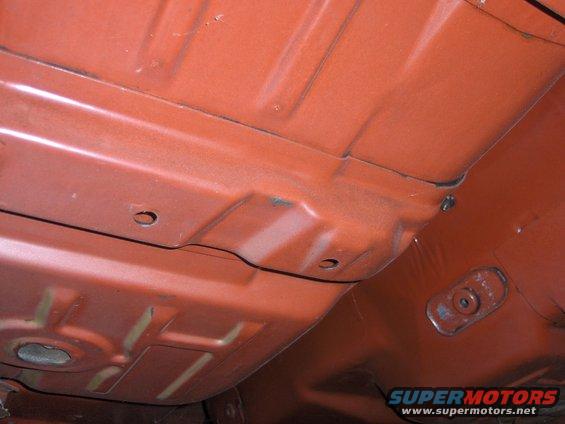 Orange car undercarriage with visible structural beams and bolt holes