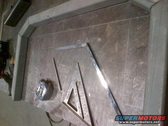 Metal fabrication tools including a tape measure, pencil, and squares on a workbench with metal tubing