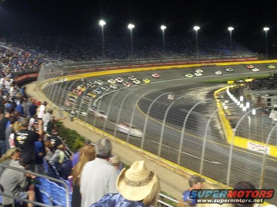 stock cars racing at night on a track with spectators in the stands
