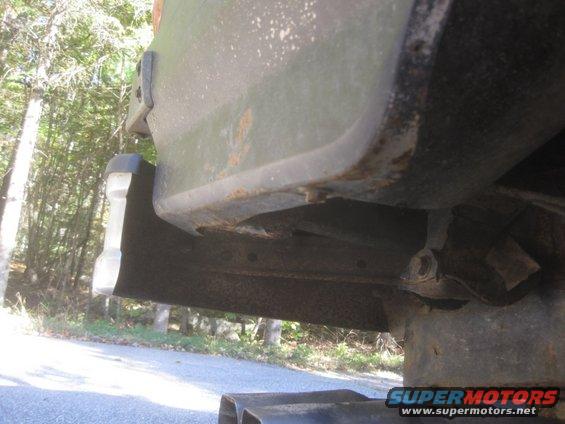 Close-up of a rusted vehicle frame and bumper corner with trees in the background