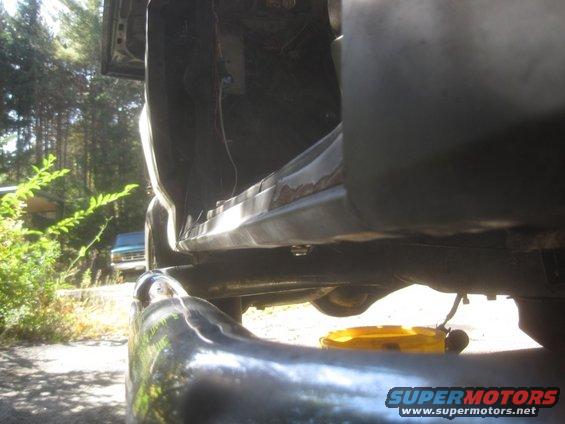 Close-up of a rusty rocker panel and interior of a vehicle, with a yellow oil drain pan underneath