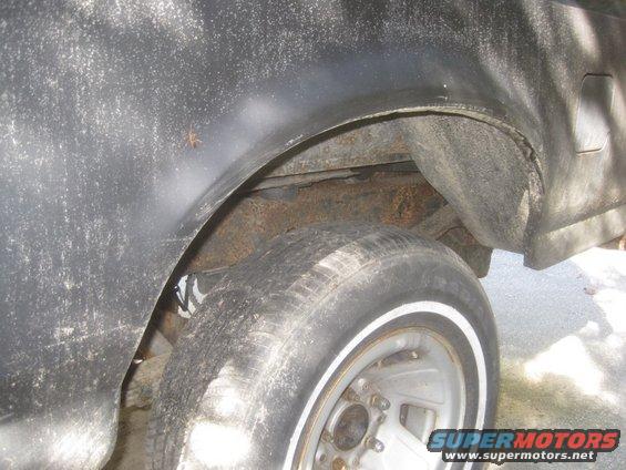 Black vehicle's rusty rear wheel well and tire with whitewall trim