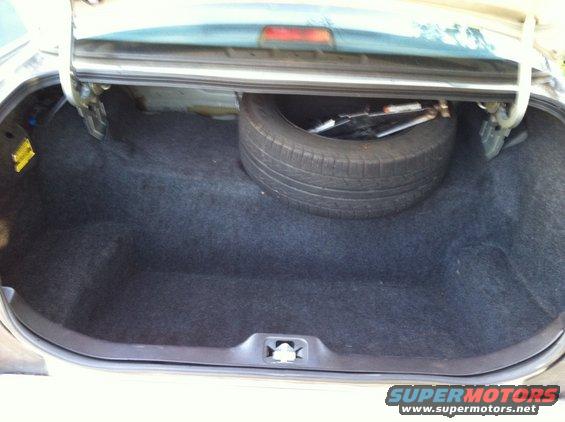 Car trunk open showing spare tire and jack. Watermark 'SUPERMOTORS www.supermotors.net' at bottom right