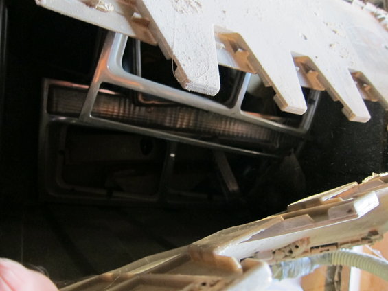 Close-up of a vehicle's front grille and headlight assembly, partially obscured by wooden planks