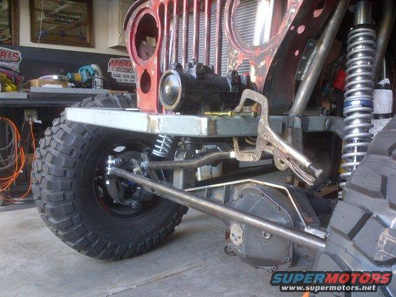 Red Jeep CJ-series front end with large off-road tires, custom suspension, and a clamp on the frame