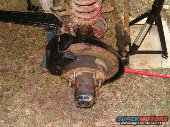 close-up of a vehicle's front wheel hub, brake rotor, caliper, and suspension spring