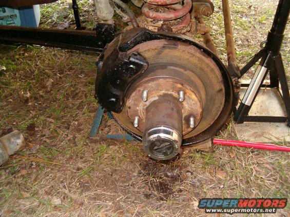 Vehicle brake rotor and hub assembly with black caliper, supported by jack stands on grassy ground