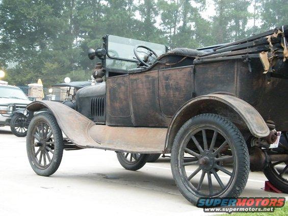 Rusty brown antique car with a black top, seen from the side at a slight front angle