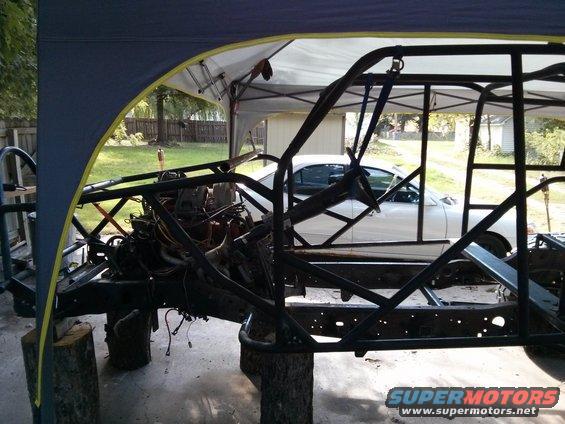 Vehicle chassis and engine under a canopy, with a white car visible in the background