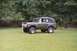 1976 Ford Bronco - A 1976 Ford Bronco is seen from a 3/4 front angle on a grassy field, with a driver behind the wheel.
