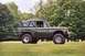 1976 Ford Bronco - A side view of a green 1976 Ford Bronco with a black soft top, positioned on a grassy field.