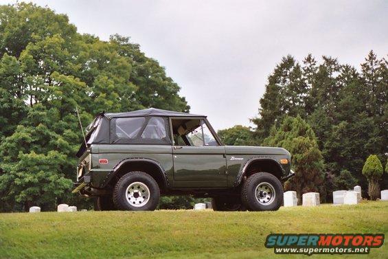 Green 1976 Ford Bronco parked on a grassy hill with trees and gravestones