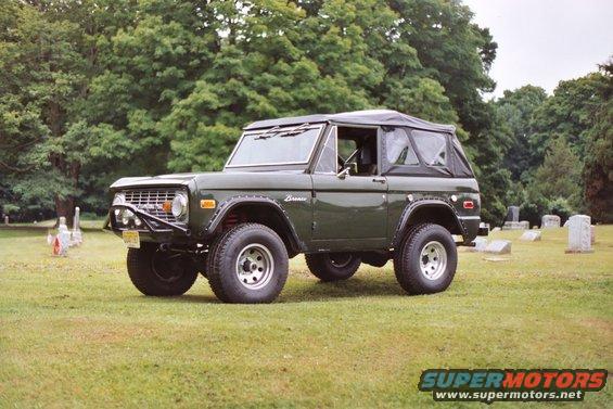 Dark green 1976 Ford Bronco with a soft top and aftermarket bumper parked on grass