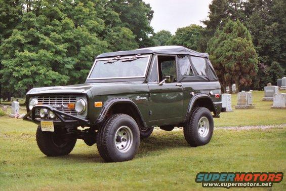 Dark green 1976 Ford Bronco with a soft top parked in a cemetery