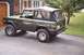 1976 Ford Bronco - 1976 Ford Bronco in dark green with a black soft top, parked in front of a house.