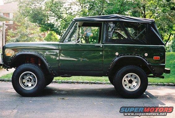 Green 1976 Ford Bronco with a black soft top, side view, parked on asphalt