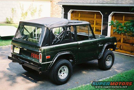 Dark green Ford Bronco parked in driveway, soft top on, roll cage visible inside