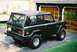 1976 Ford Bronco - A dark green Ford Bronco with a soft top is parked in front of a garage.