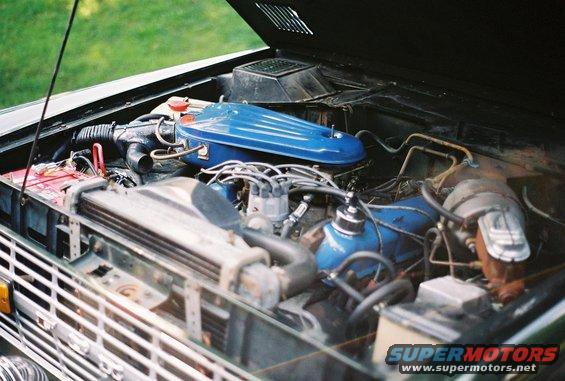 Engine bay of a 1976 Ford Bronco, showing the V8 engine with blue valve covers and air cleaner, radiator, and battery