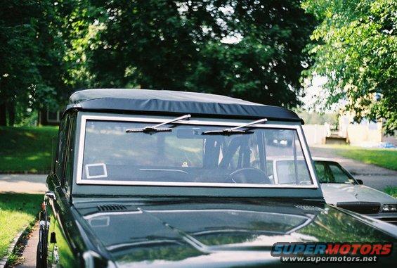 1976 Ford Bronco front view, dark green with black soft top. Another car is parked behind it