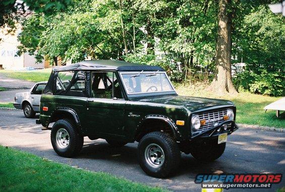 Green Ford Bronco parked on a street, another car behind it