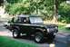 1976 Ford Bronco - A dark green Ford Bronco is parked on a paved surface with grass and trees in the background.