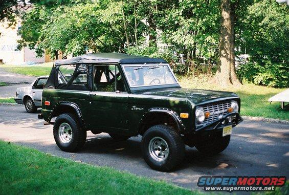 Dark green 1976 Ford Bronco with a soft top parked on a driveway. Another car is visible in the background