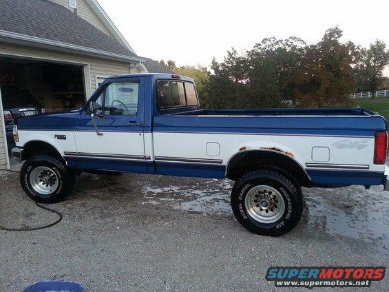 Blue and white Ford F-250 pickup truck, side view, showing rust on rear fender, parked in driveway