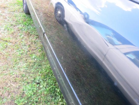 Black car side panel reflecting another vehicle, showing grass and sky
