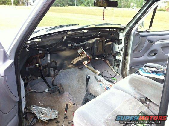 Disassembled dashboard of a light-colored truck, showing exposed wires and components. Tools are on the floor