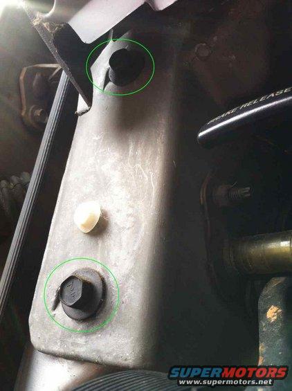 Close-up of a metal bracket in an engine bay, showing two bolts circled in green