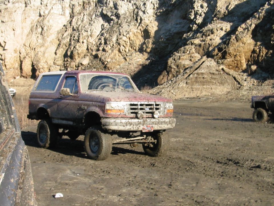 Lifted muddy two-tone Ford Bronco on big tires parked in a rocky mud pit