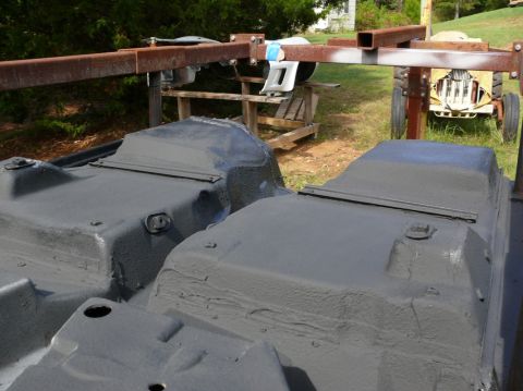 Two gray car underbodies on a metal stand outdoors