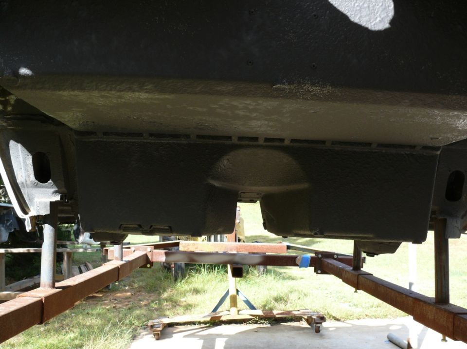 Underside of a dark-colored vehicle on a trailer, showing frame and suspension components