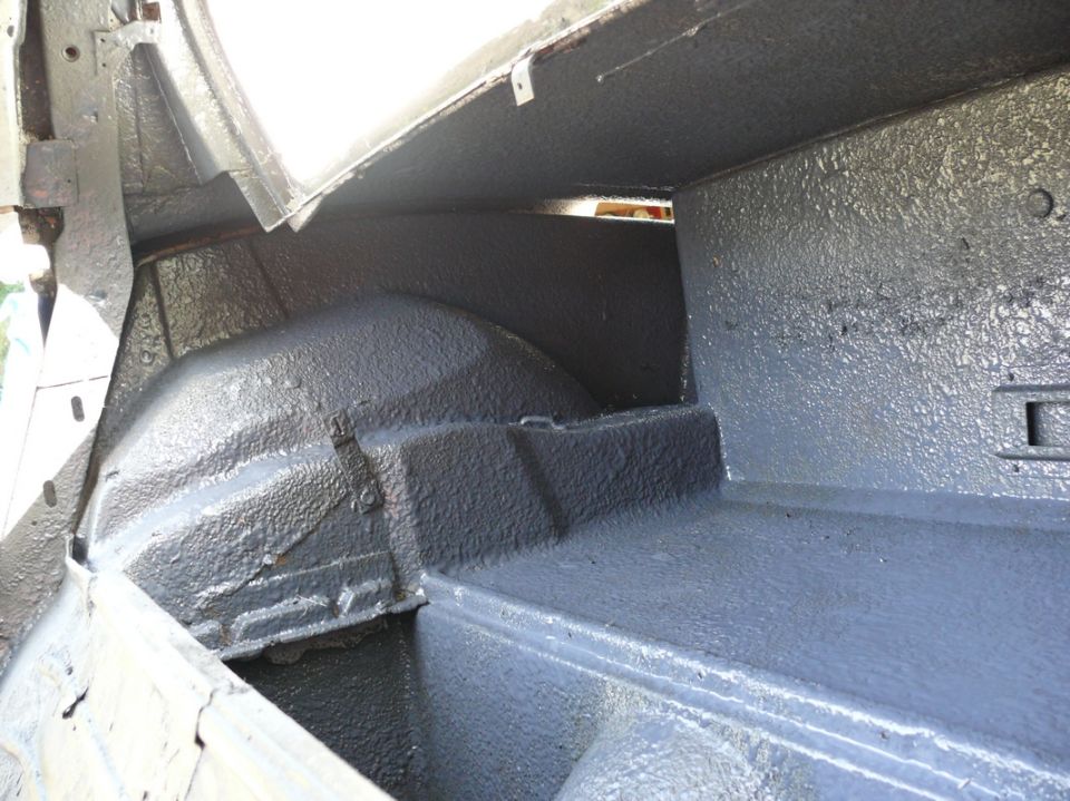 Interior of a car trunk, showing the wheel wells and floor coated in dark grey material