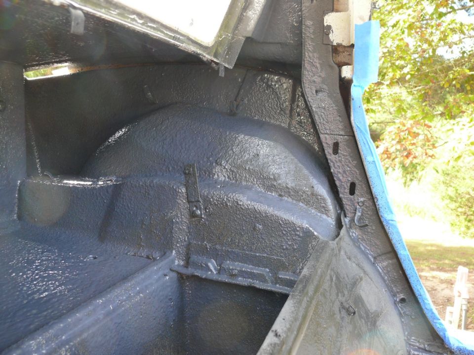 Inside of a car's trunk area, showing the rear wheel well and freshly painted surfaces. Blue tape is visible on the right side