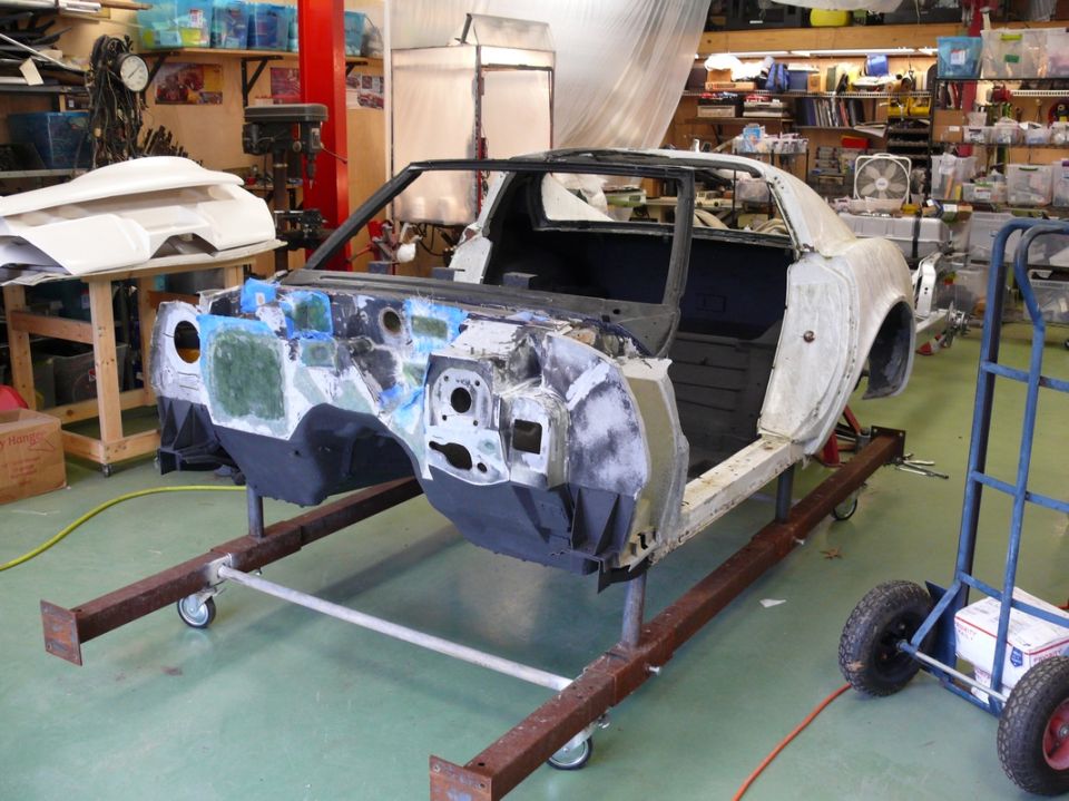 Car body on a stand in a workshop, looks like a 1976 Chevrolet Corvette