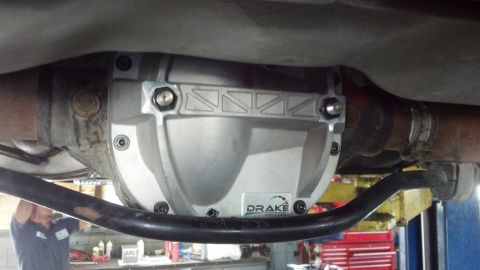 2003 Ford Crown Victoria - Underbody view of a cast aluminum Drake differential cover installed on a rear axle, with exhaust and sway bar visible on a shop lift.