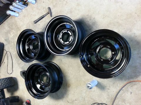 1982 Jeep Wagoneer - A collection of black steel wheels are laid out on a concrete surface, accompanied by spray paint and tools.