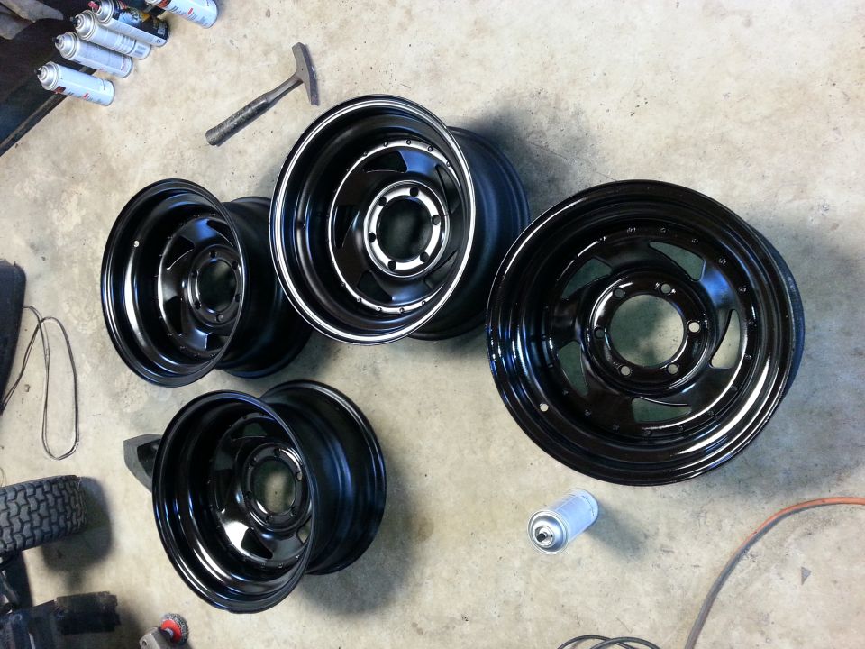 Four black steel wheels and one spare wheel on a concrete floor with spray paint cans and a hammer