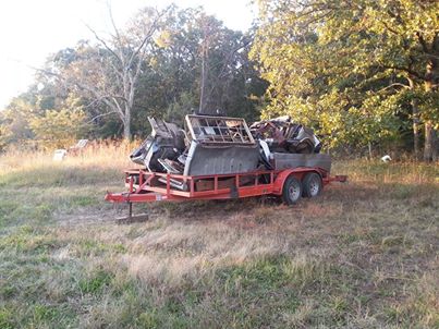 1995 Ford F-150 - A trailer filled with various metal pieces and car parts sits in a dry, grassy area with trees in the background.
