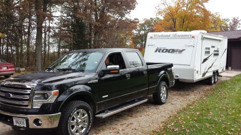 1978 Ford Bronco - A black Ford F-150 pickup truck tows a white travel trailer on a gravel driveway.