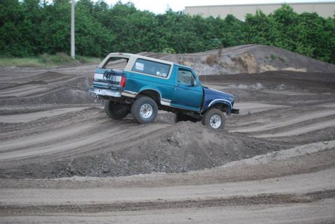 1996 Ford Bronco - A teal and white Ford Bronco navigates a dirt track with multiple mounds and ruts.