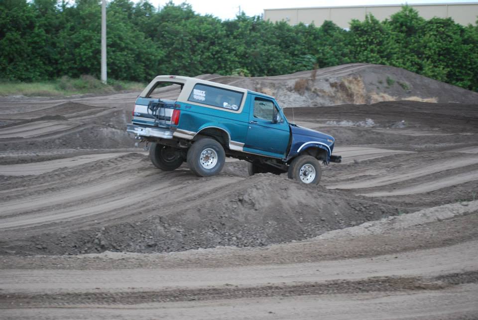 Teal and white Ford Bronco driving on a dirt track, angled to the right