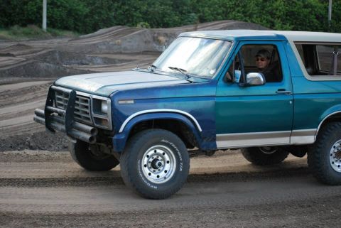 1996 Ford Bronco - A blue Ford Bronco with a tan top is shown from the front three-quarter view on a dirt track.